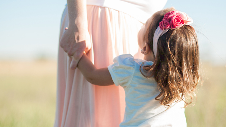 little girl with pink headband looks up at mother holding her hand