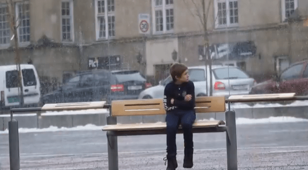 A freezing child sits at a bus station in Oslo, Norway.