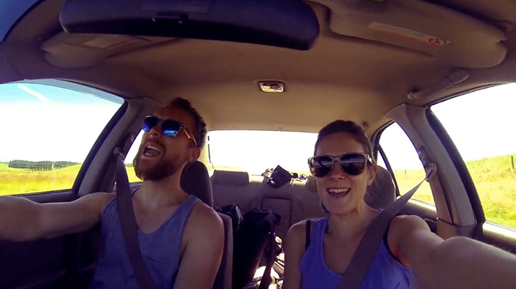 Young world travelling couple inside car singing