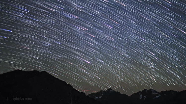 Timelapse image of meteors through night sky over mountains.