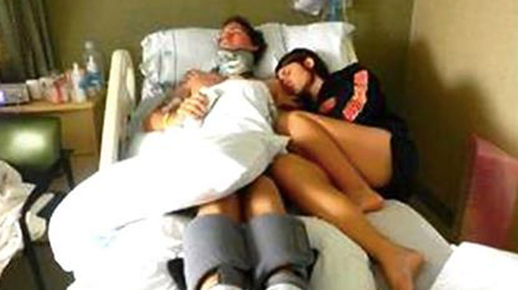 wife lays next to husband on hospital bed