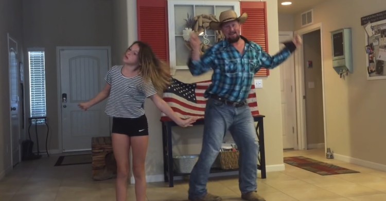 young girl and her dad dancing together. dad is wearing a cowboy hat and boots.