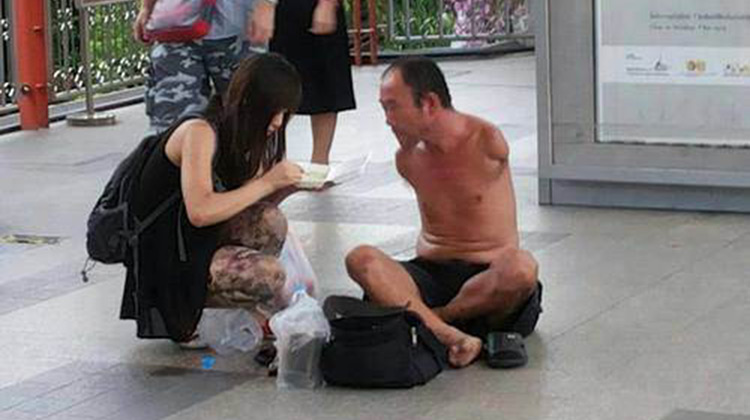 Woman feeding homeless man with no arms