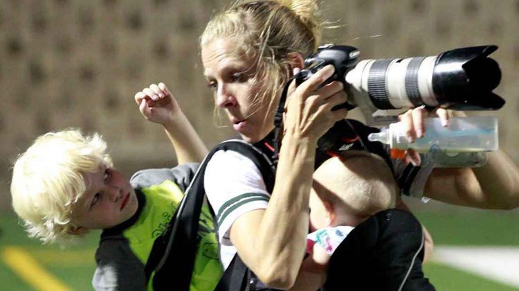mom holding camera with baby strapped in front and little boy strapped to back