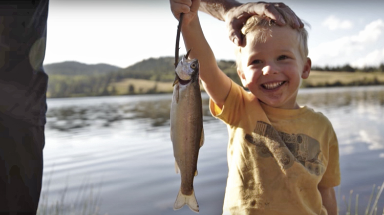 little boy holding up fish he caught with dad's hand resting on head