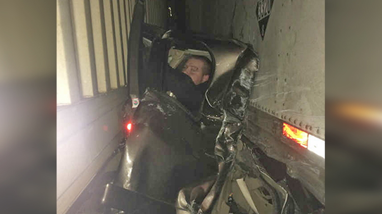 man in crushed truck between 2 semis