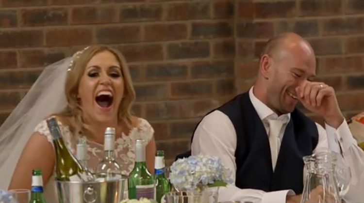 a bride and groom laughing as they sit at a table during their reception.