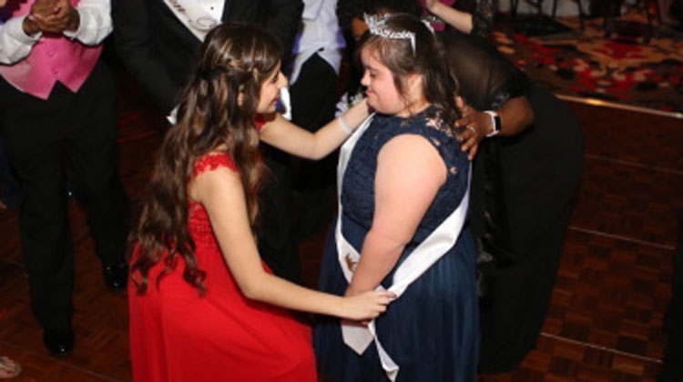 girl in red dress bends down to girl with crown
