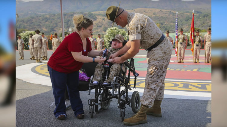 little boy in wheelchair attended by mother and marine