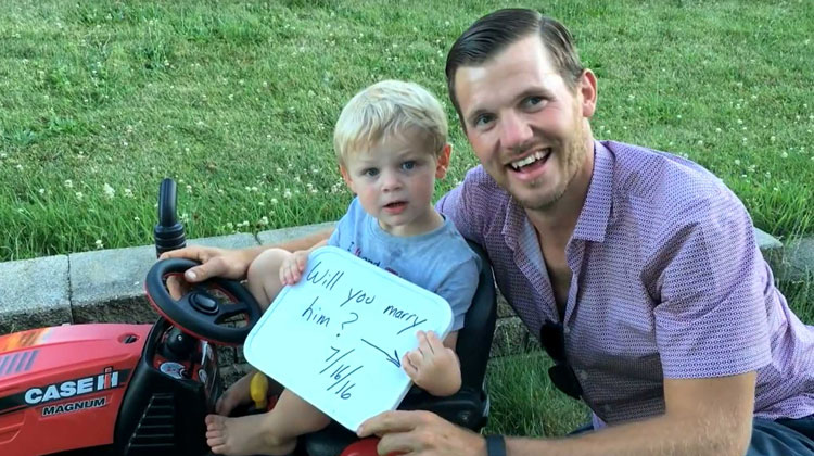 man in plaid holding whiteboard with little boy on tractor