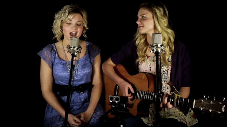 sisters sing in front of microphones sitting on stools