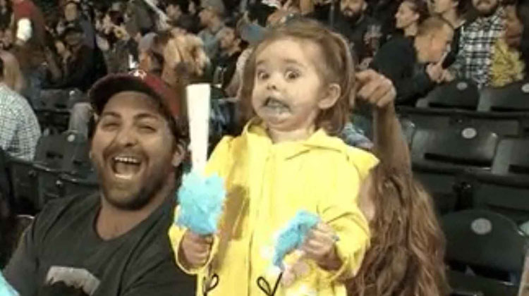 little girl in yellow tries blue cotton candy with astounded face