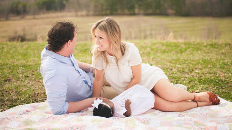 woman, man and baby laying on blanket. woman looking into mans eyes