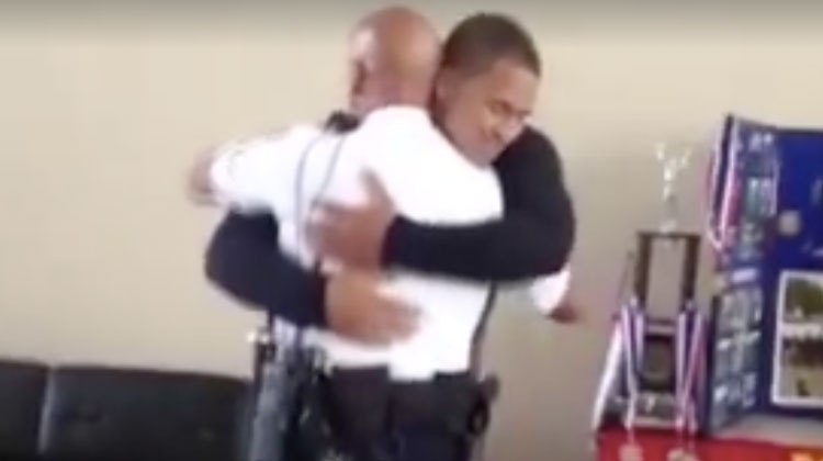 man in black hugs police officer in white