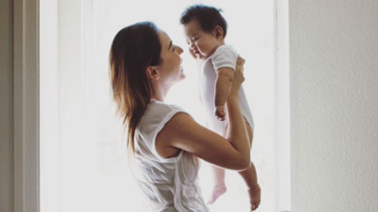 mom holds up baby all in white