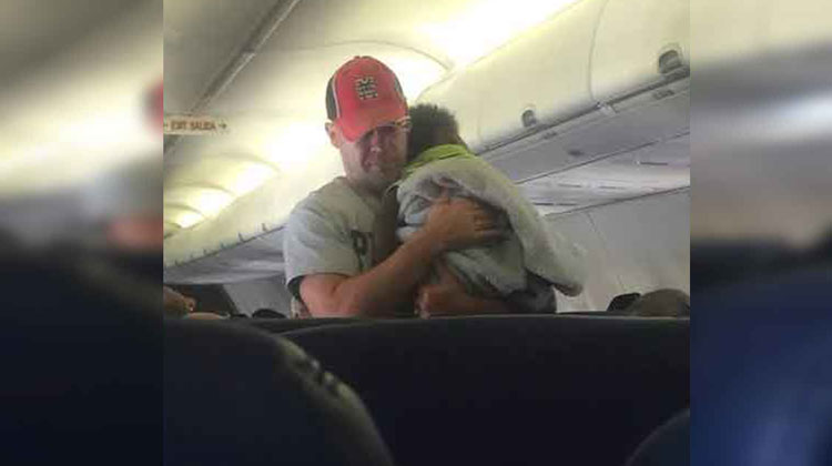 man in baseball hat carrying small baby on plane