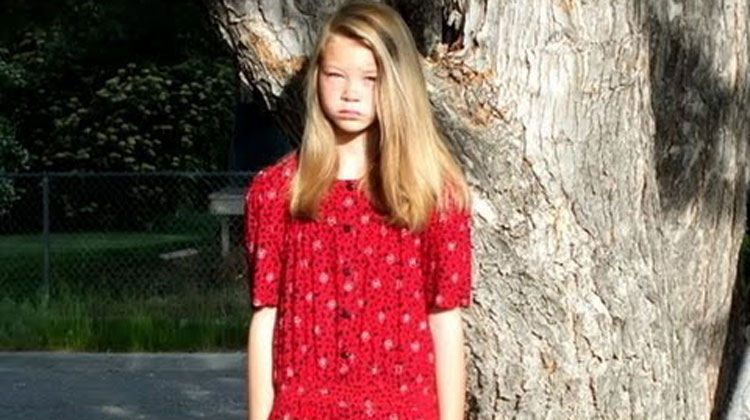 young girl in red short sleeve romper in front of tree