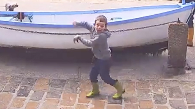 little boy in hoody dances in front of boat
