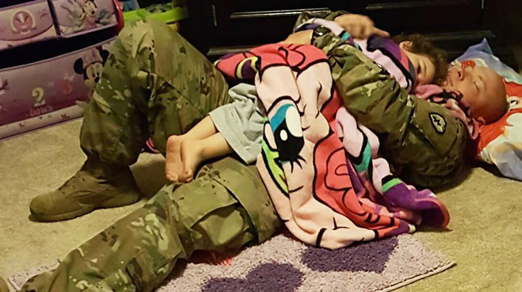 man in military camo holds girl in pink unicorn blanket
