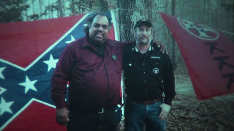 black and white man standing in front of confederate and kkk flags