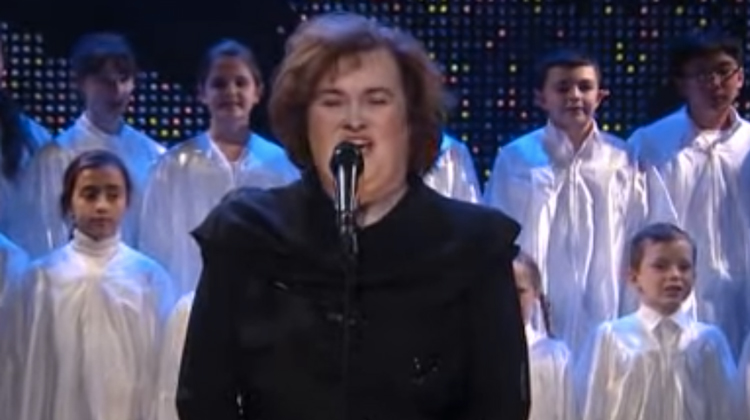 susan boyle in black singing with white robed childrens choir in background
