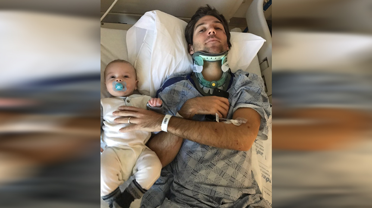 man in neckbrace on hospital bed with baby