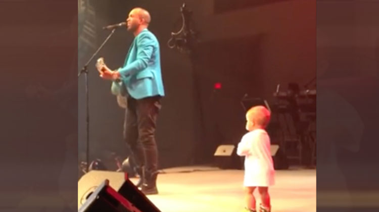 man playing guitar on stage with little boy in white shirt watching him