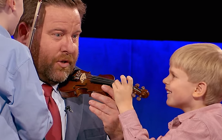 shane jacobson holding tiny violin