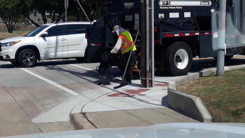 city worker fills hole in crosswalk
