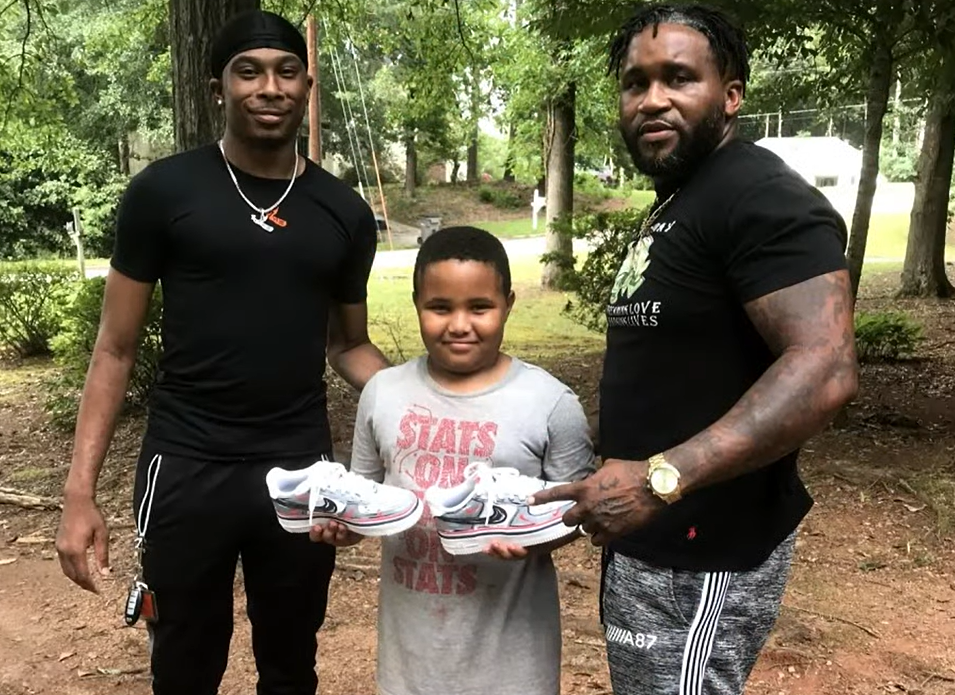 little boy holding shoes with two men smiling beside him