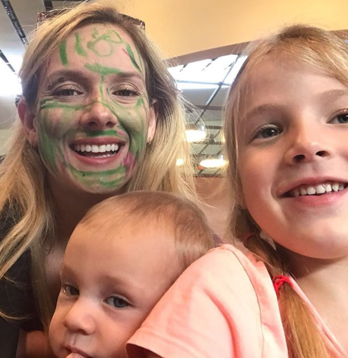 woman with face covered in maker smiling with two children