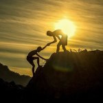 one person helping another up a mountain at sunset