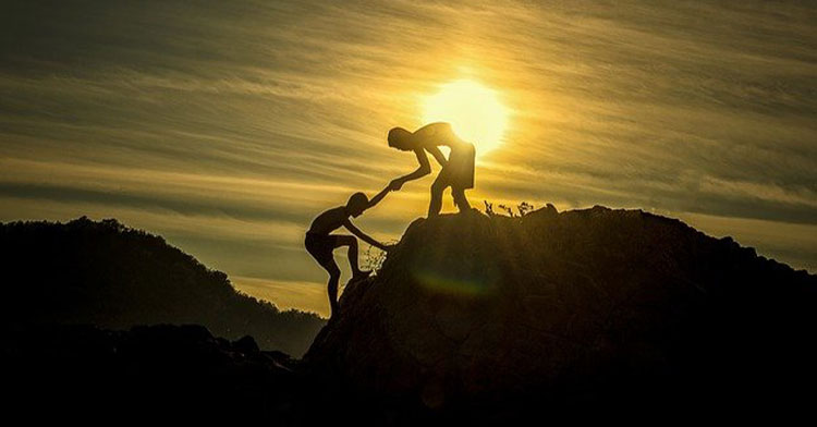one person helping another up a mountain at sunset