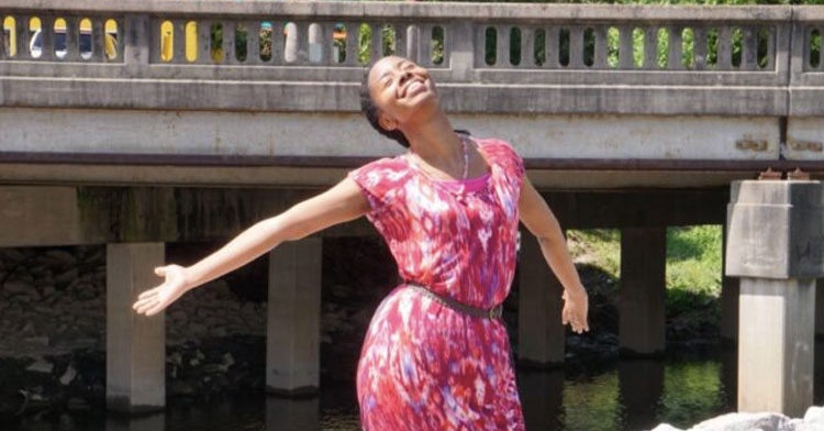 woman smiling in pink dress with her arms stretched wide