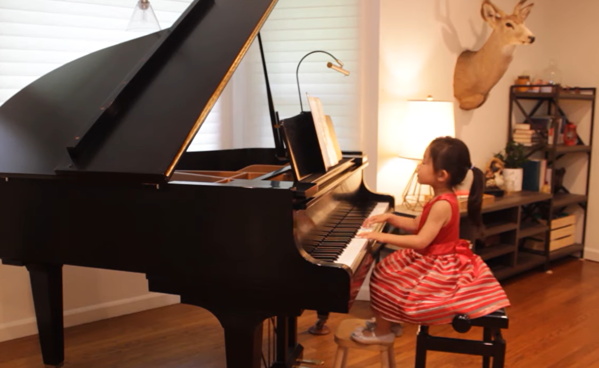 4-year-old playing piano in red dress with feet on tiny stool