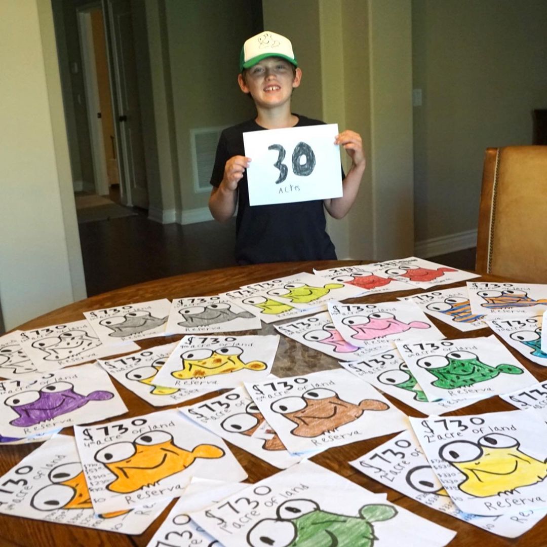 little boy holding sign that reads 30 acres next to fundraising posters of frogs