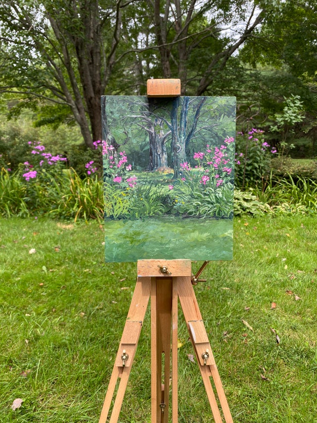 artist's easel holding painting of purple flowers in garden.