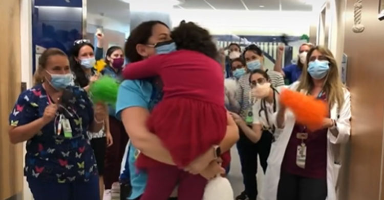 little girl hugging nurse with other nurses cheering behind them
