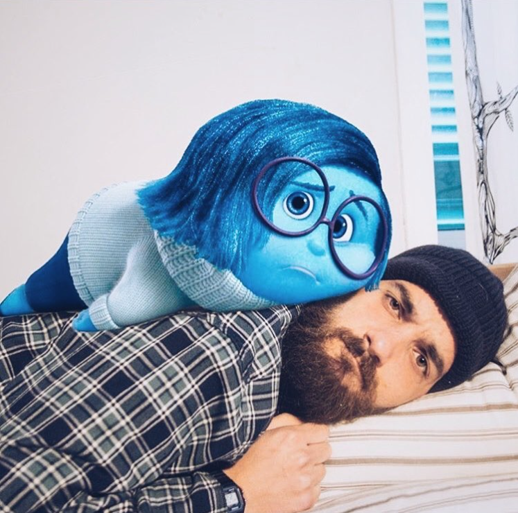 man laying on a bed with a photoshop version of sadness from the disney movie inside out