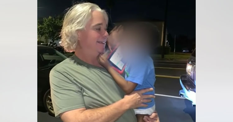 delivery driver holding little boy whose face is blurred out of picture