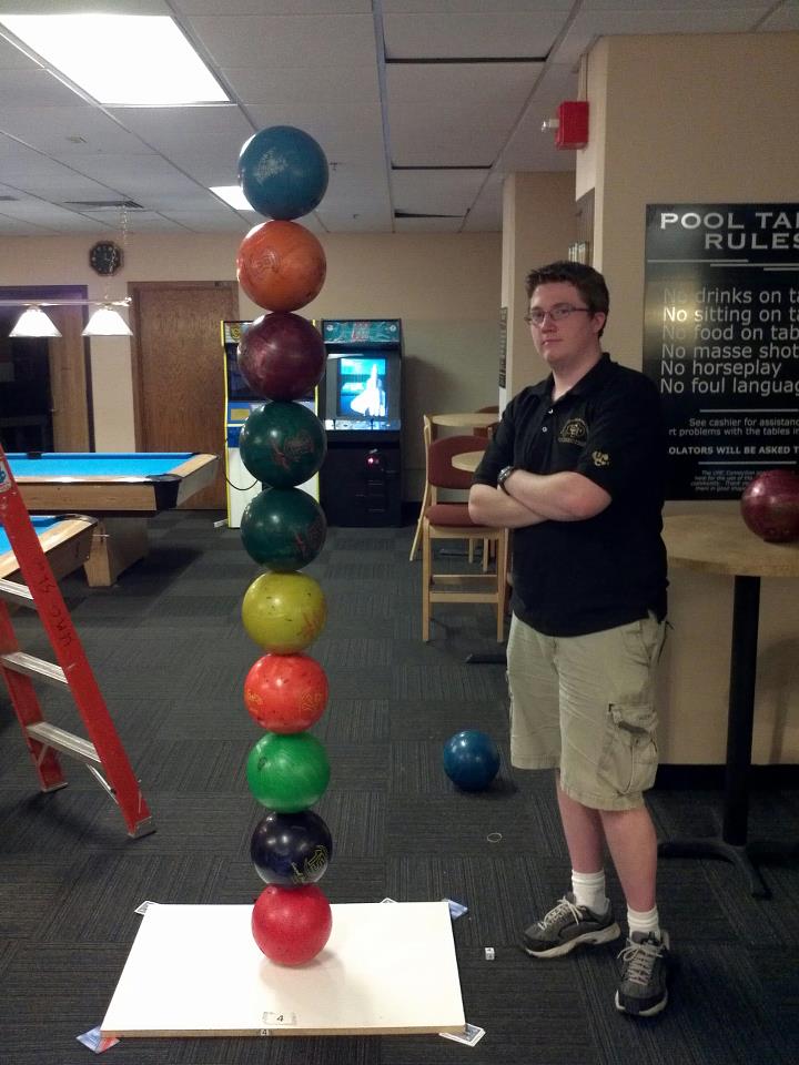 a young man balanced 10 bowling balls on top of each other