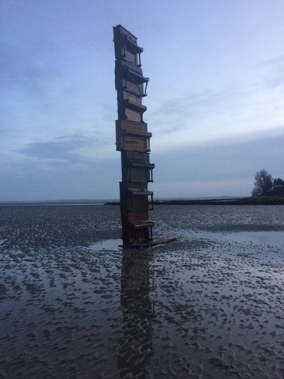 7 upright pianos balanced on top of each other on a beach