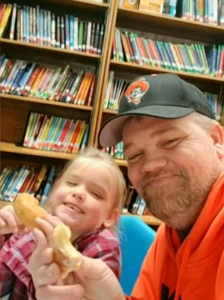 man and little girl holding donuts and smiling in a library