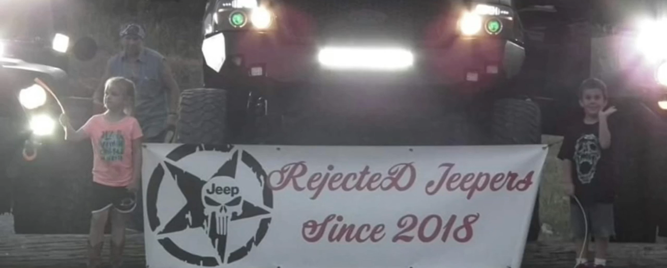 little girl and boy holding up a sign that says "rejeceted jeepers since 2018" while standing in front of jeeps