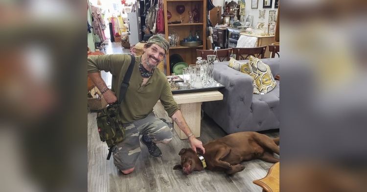 man crouched next to brown dog in thrift store
