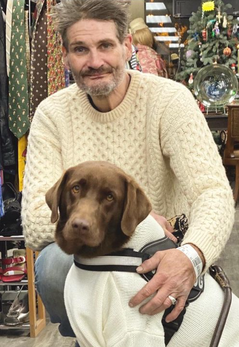 man wearing a sweater squatting behind a dog in a sweater 