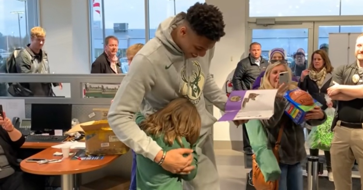 giannis antetokounmpo hugging a little girl and holding a folder in one hand with a crowd of people watching and taking pictures