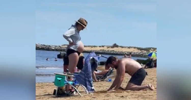 man digs hole in sand for wife's baby bump at the beach