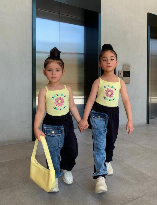 two little girls wearing matching outfits and holding hands while walking away from an elevator door