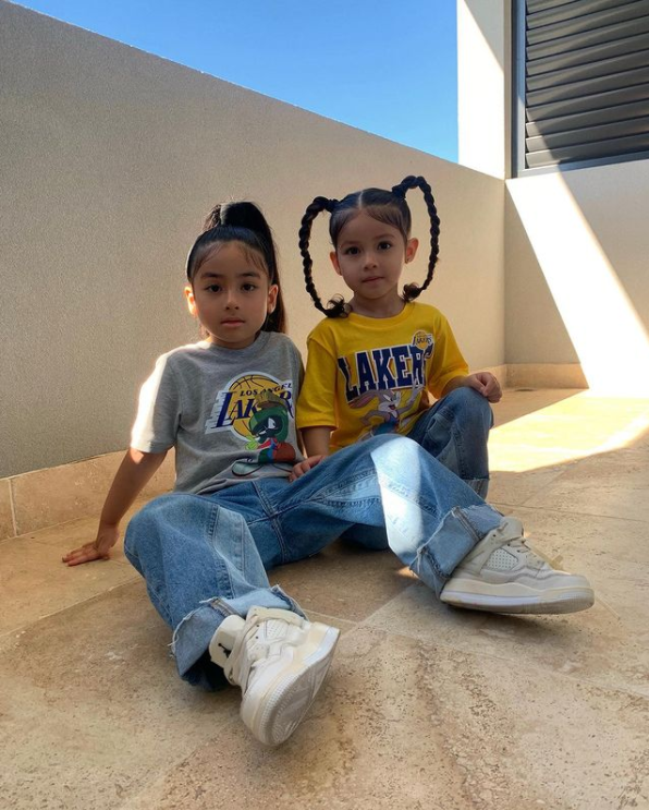 two little girls sitting on the ground outside while wearing lakers shirts